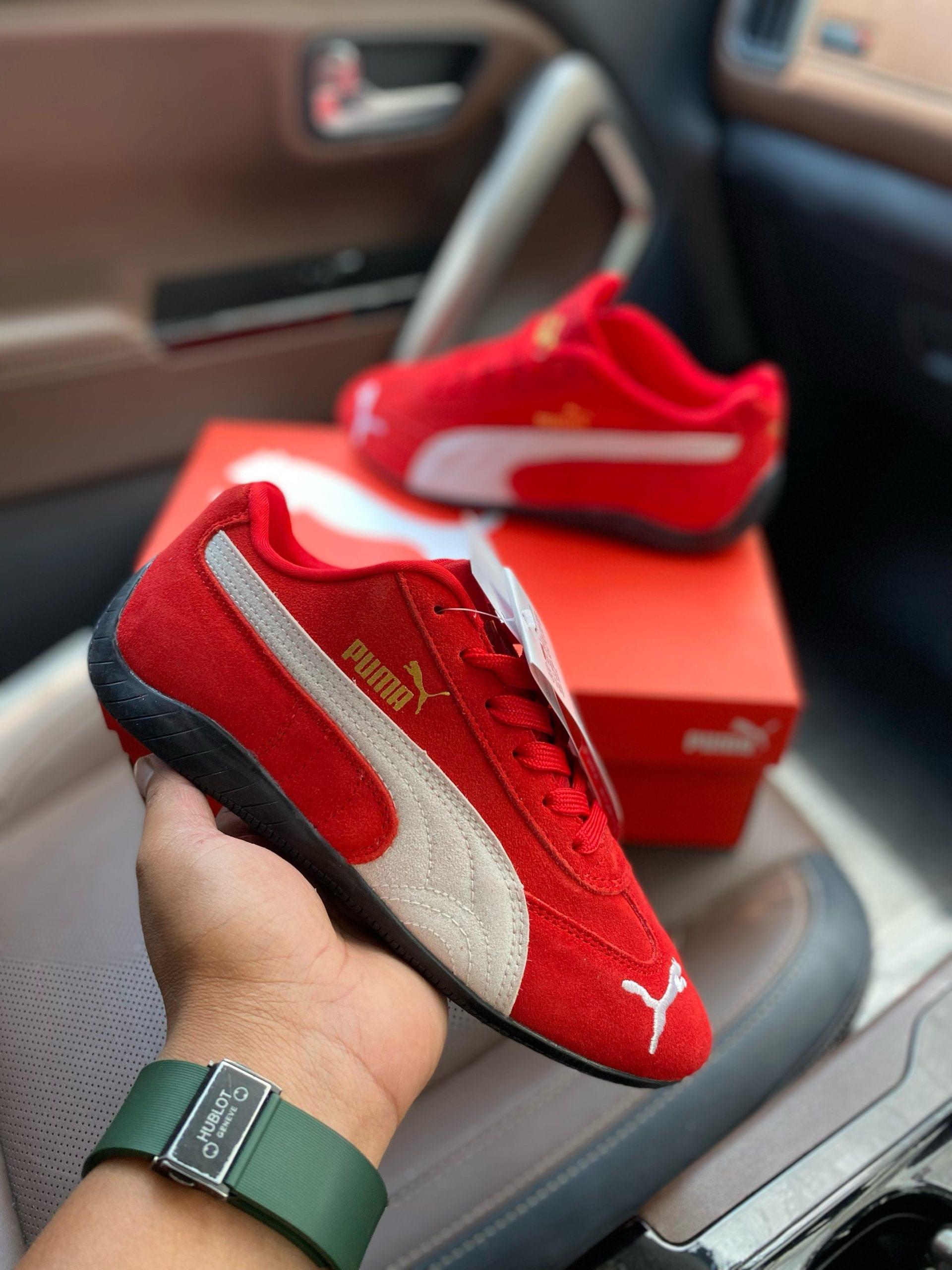 Hand holding Puma Speedcat red and white first copy shoes in a car with original box