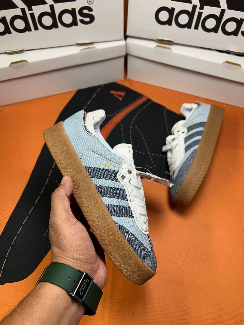 Adidas Sambae X Atmos Denin First Copy Shoes in denim blue with gum sole held in hand in front of Adidas shoe boxes